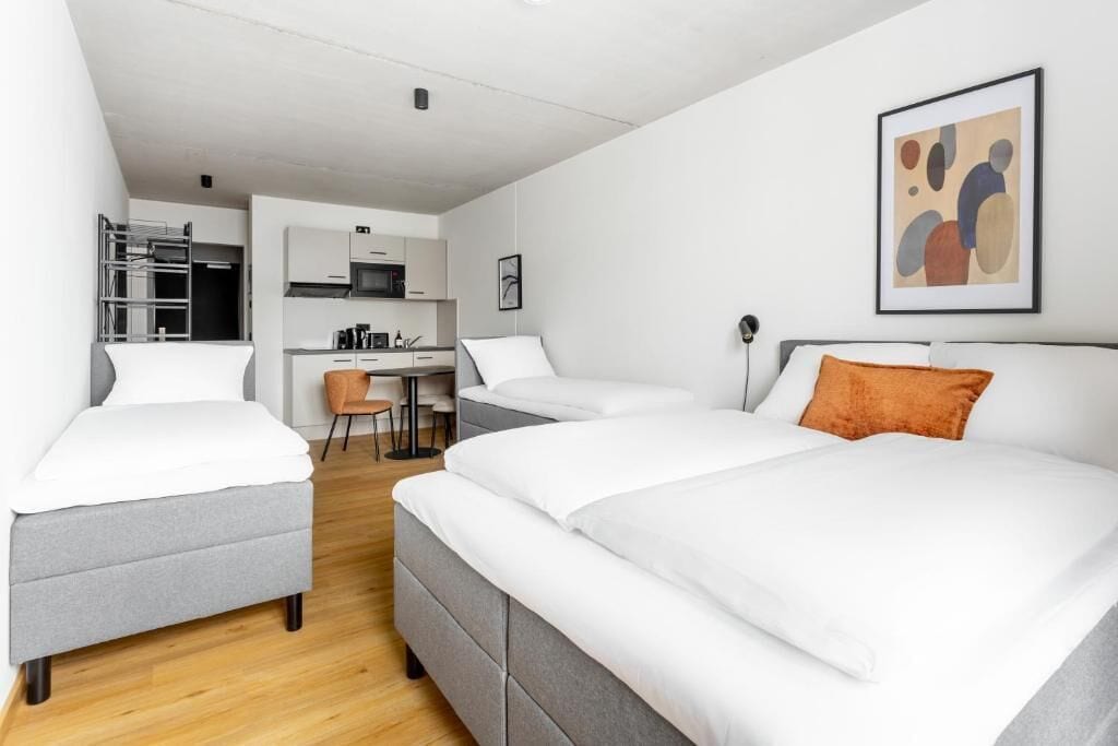 Ein modernes Hotelzimmer mit zwei Betten, einem Schreibtisch und einer Küchenzeile.