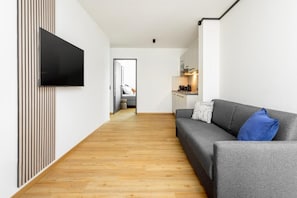 A modern living room with a grey sofa, a flat-screen TV mounted on the wall, and a wooden floor.