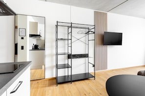 A modern kitchen with a black metal shelving unit, a flat-screen TV mounted on the wall, and a wooden floor.