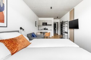 A modern hotel room with a bed, a desk, and a kitchenette.