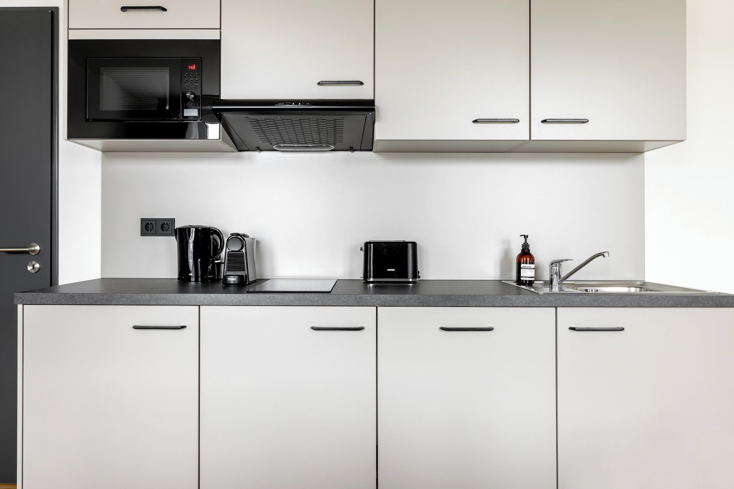 Eine moderne Küche mit weißen Schränken, einer schwarzen Mikrowelle, einer Kaffeemaschine, einem Toaster und einem Waschbecken mit Armatur.