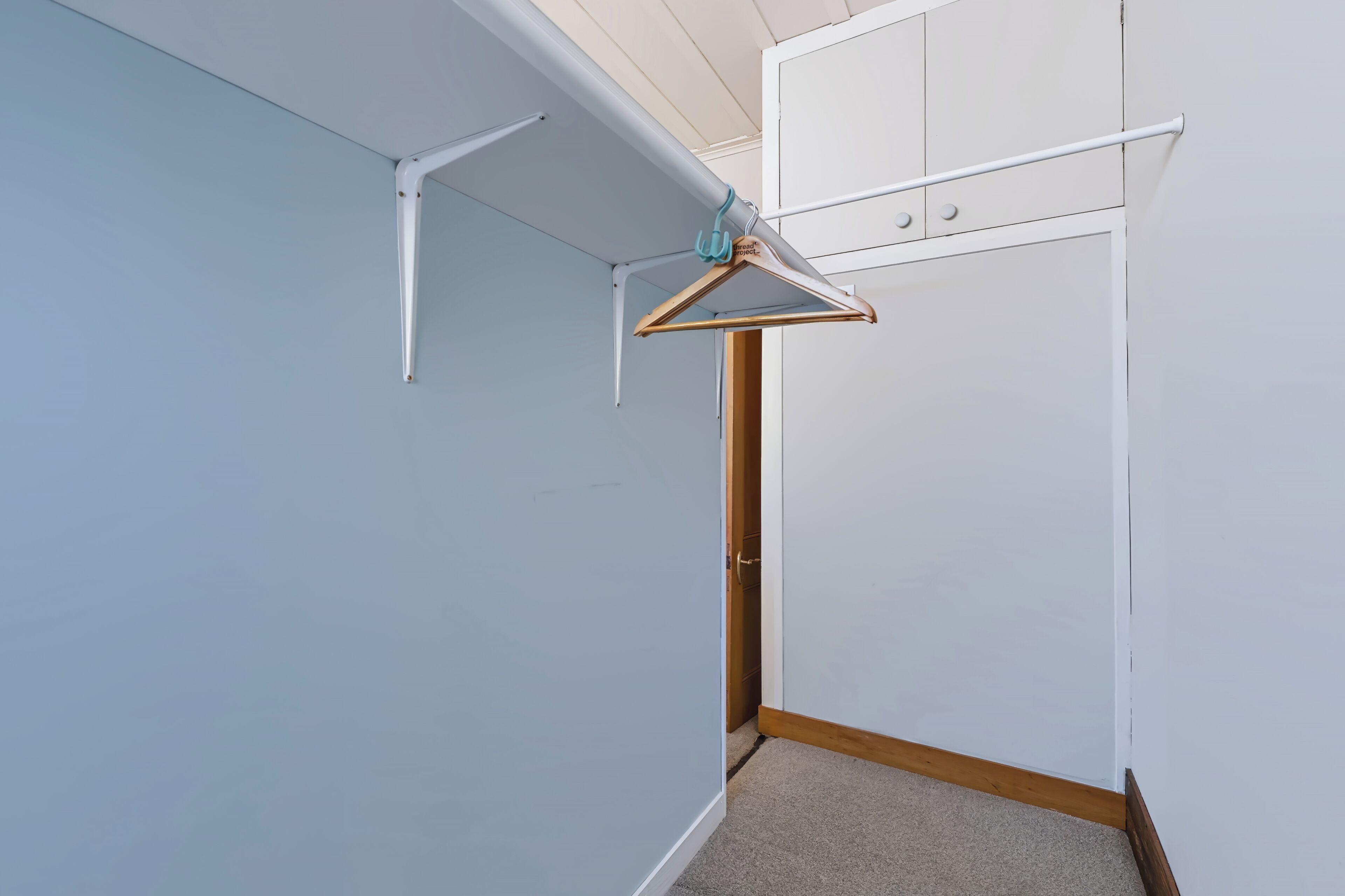 Esquina de una habitación con una puerta blanca, suelo de madera y pared blanca.