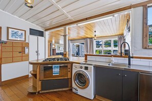 A modern kitchen with a built-in washer, a wooden countertop, and a large window. - Hannan House - Whitianga Holiday Home (Whitianga)