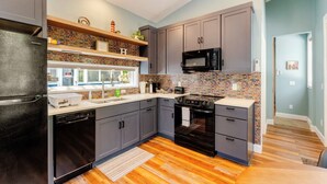 Una cocina moderna con armarios grises, un refrigerador negro, un microondas y un salpicadero con diseño de ladrillo.