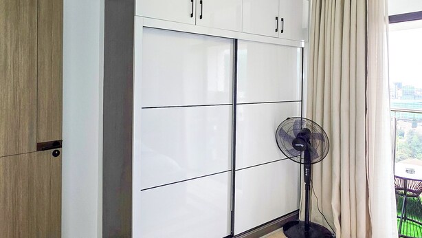 A bedroom with a bed, a wardrobe, a standing fan, and a view of greenery outside. - One Bedroom in Westlands close to GTC, JW Mariott,Sarit Centre,Aga Khan Hospital (Nairobi)