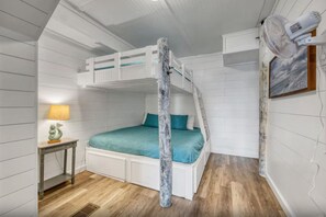 Ein Schlafraum mit Etagenbetten, einer weißen Decke, einem Nachttisch mit Lampe und einem an der Wand befestigten Ventilator.