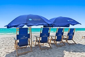Strandstole og parasoller med 'GREEN REEF' mærke på en sandstrand.