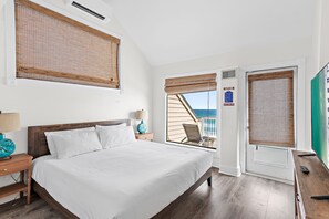 Ein Schlafzimmer mit Bett, Nachttisch, Lampe, Fenster mit Blick und einer Tür mit Schild.