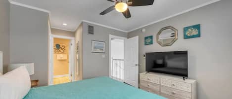 A bedroom with a bed, a ceiling fan, a TV on a dresser, and a door leading to another room.