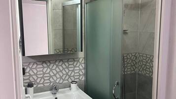 Une salle de bain avec un lavabo blanc, un miroir, un espace douche et un mur recouvert de carreaux décoratifs.
