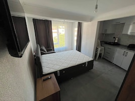 Una habitación compacta con cama, un escritorio pequeño, kitchenette y ventana con cortinas.