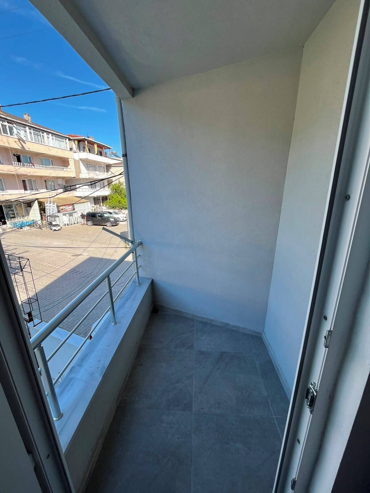 A balcony with a metal railing, a door, and a view of a building with multiple floors and balconies.