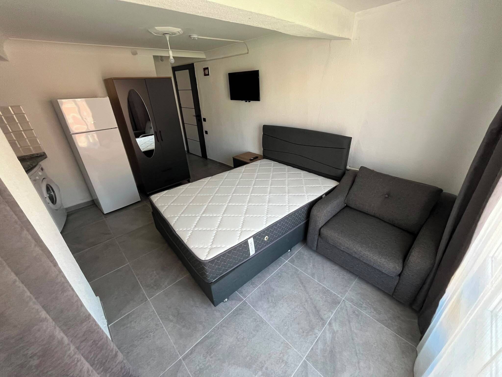 A compact room with a bed, a sofa, a television, and a washing machine.