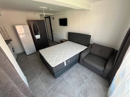 Una habitación compacta con cama, sofá, televisión y lavadora.