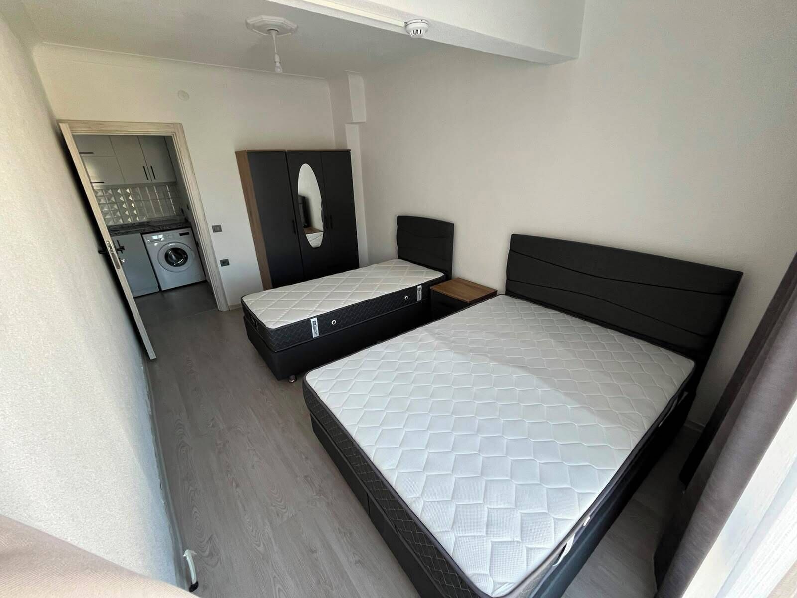 Une chambre compacte comprenant un lit, une petite table de chevet, une armoire et un lave-linge dans la pièce adjacente.