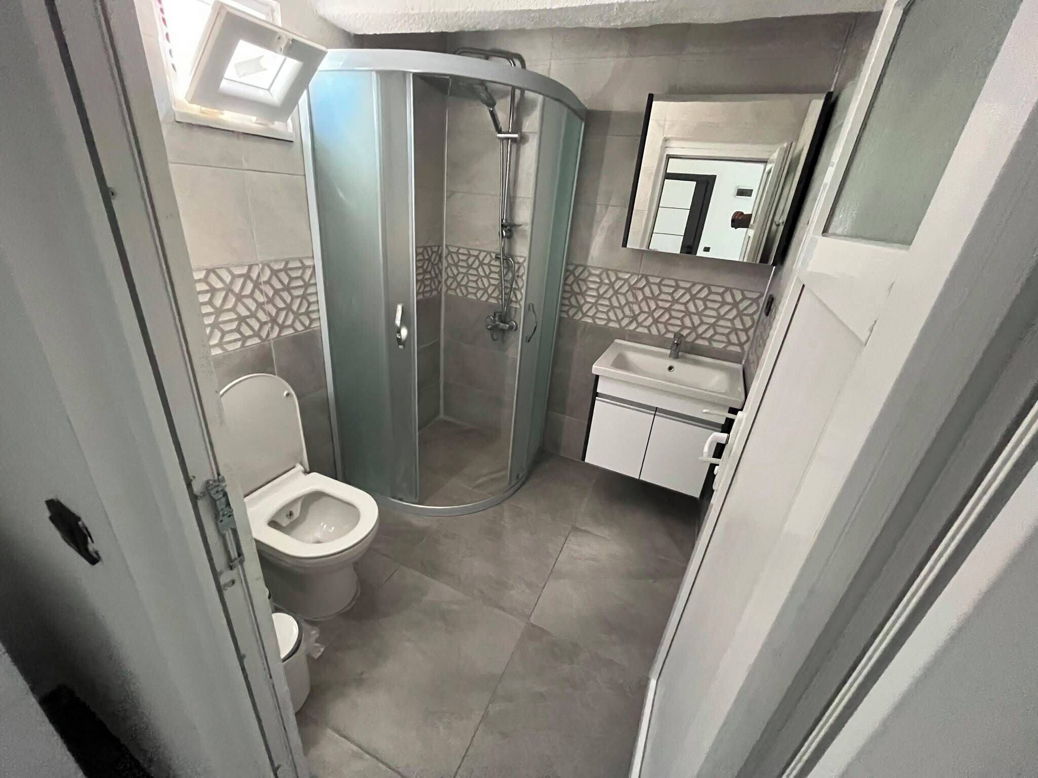 Een kleine badkamer met toilet, douchecabine en wastafel.
