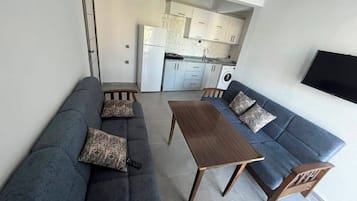 Un espacio habitable compacto con un conjunto de sofá, una mesa de comedor y un televisor montado en la pared.