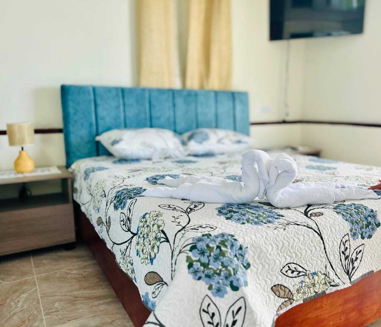 Un lit bien fait, recouvert d’une couvre-lit à motifs floraux, avec deux serviettes disposées en forme de cœur.