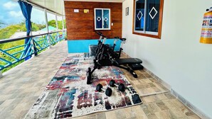 Un gimnasio con equipo de ejercicio, una alfombra estampada y vistas al exterior con vegetación.