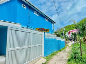 A blue house with a gated entrance, a pathway leading to a pink house, and a clear sky.