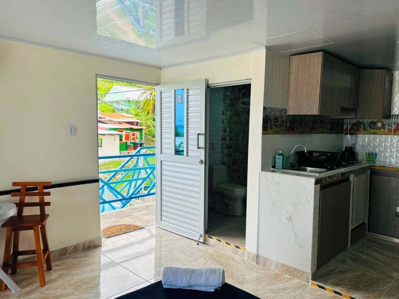 A modern kitchen with a built-in stove, a sink, and cabinets. There is a dining area with a table and chairs. A bathroom is visible through an open door.