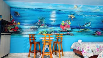 Quarto com um mural de cena subaquática, uma mesa de madeira com cadeiras e uma cama com colcha florida.