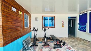Academia com bicicletas ergométricas, um banco e halteres.