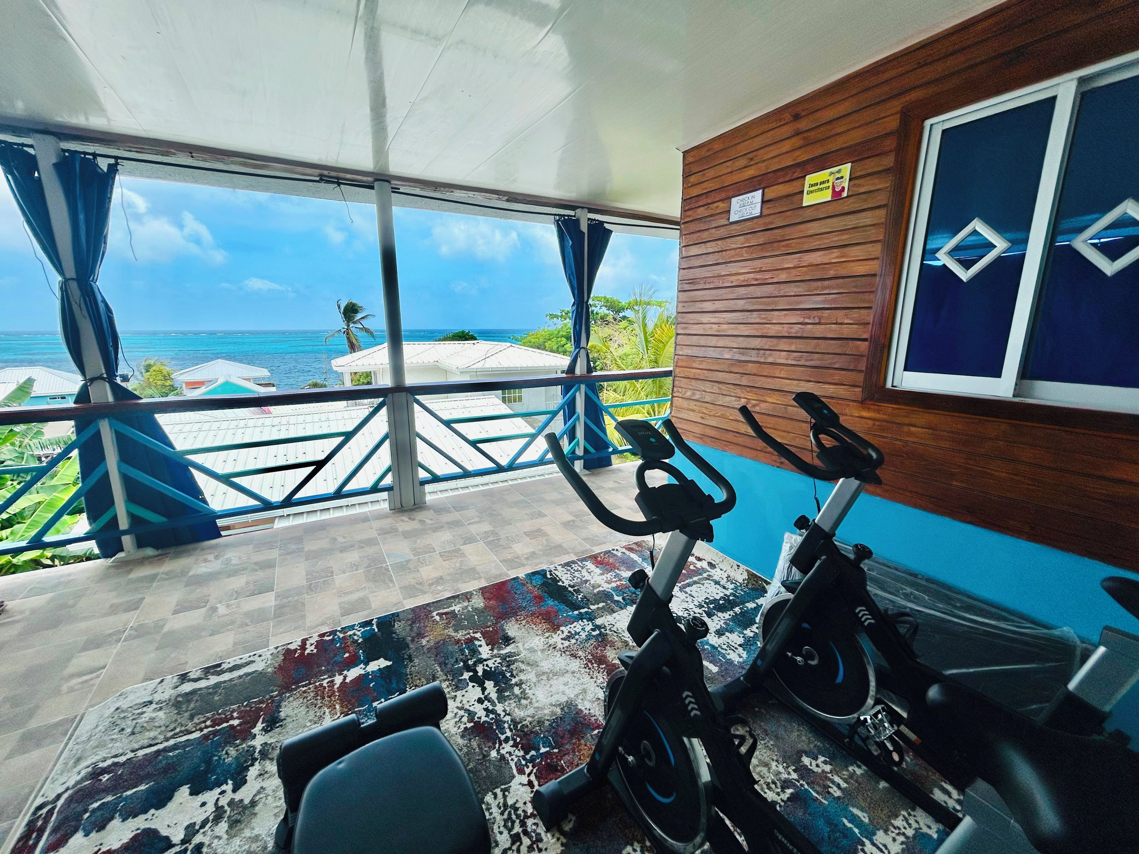A room with a view of the ocean, exercise bikes, and a wooden wall with a window.