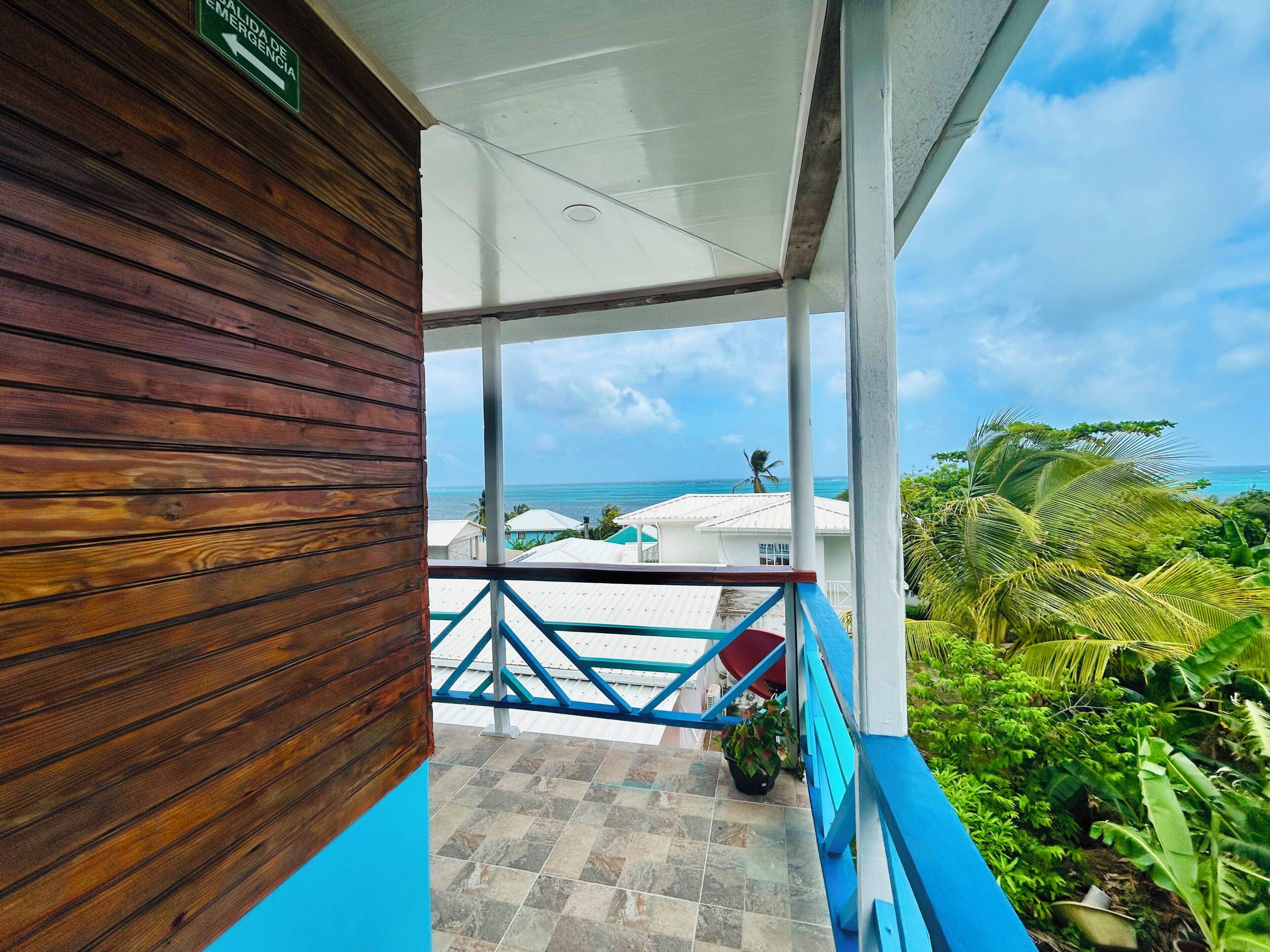 A covered outdoor area with a view of the ocean, a wooden wall, and a blue railing.
