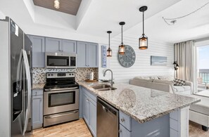 A modern kitchen with stainless steel appliances, a granite countertop, and pendant lighting. - Majestic Sun A1008•Remodeled•Pools +Hot Tubs•Views•Beach Gear•Pickleball+Tennis (Miramar Beach)