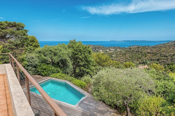 Piscina com deck de madeira, cercada por vegetação exuberante e com vista para a paisagem costeira.