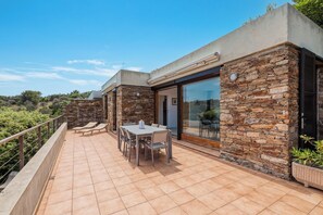 Uma casa moderna com fachada de pedra, um pátio com mesa e cadeiras, e uma porta de vidro que dá para uma área coberta.