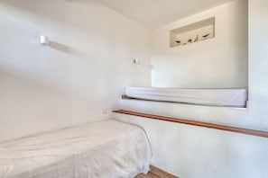 Quarto pequeno com cama de casal, prateleira de madeira e nicho fixado na parede acima da cama.
