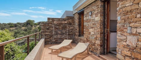A balcony with stone walls, two lounge chairs, and a view of the countryside.