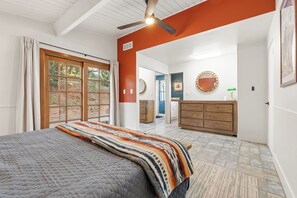 Ein Schlafzimmer mit einem Bett, einem Deckenventilator, einem großen Fenster und Blick ins Freie.
