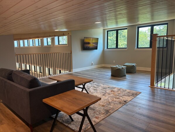 A spacious living area with a wooden ceiling, a sofa, a coffee table, and a TV mounted on the wall.