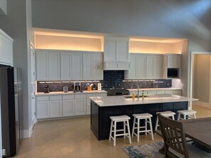 A modern kitchen with white cabinets, a central island with stools, and a built-in stove.