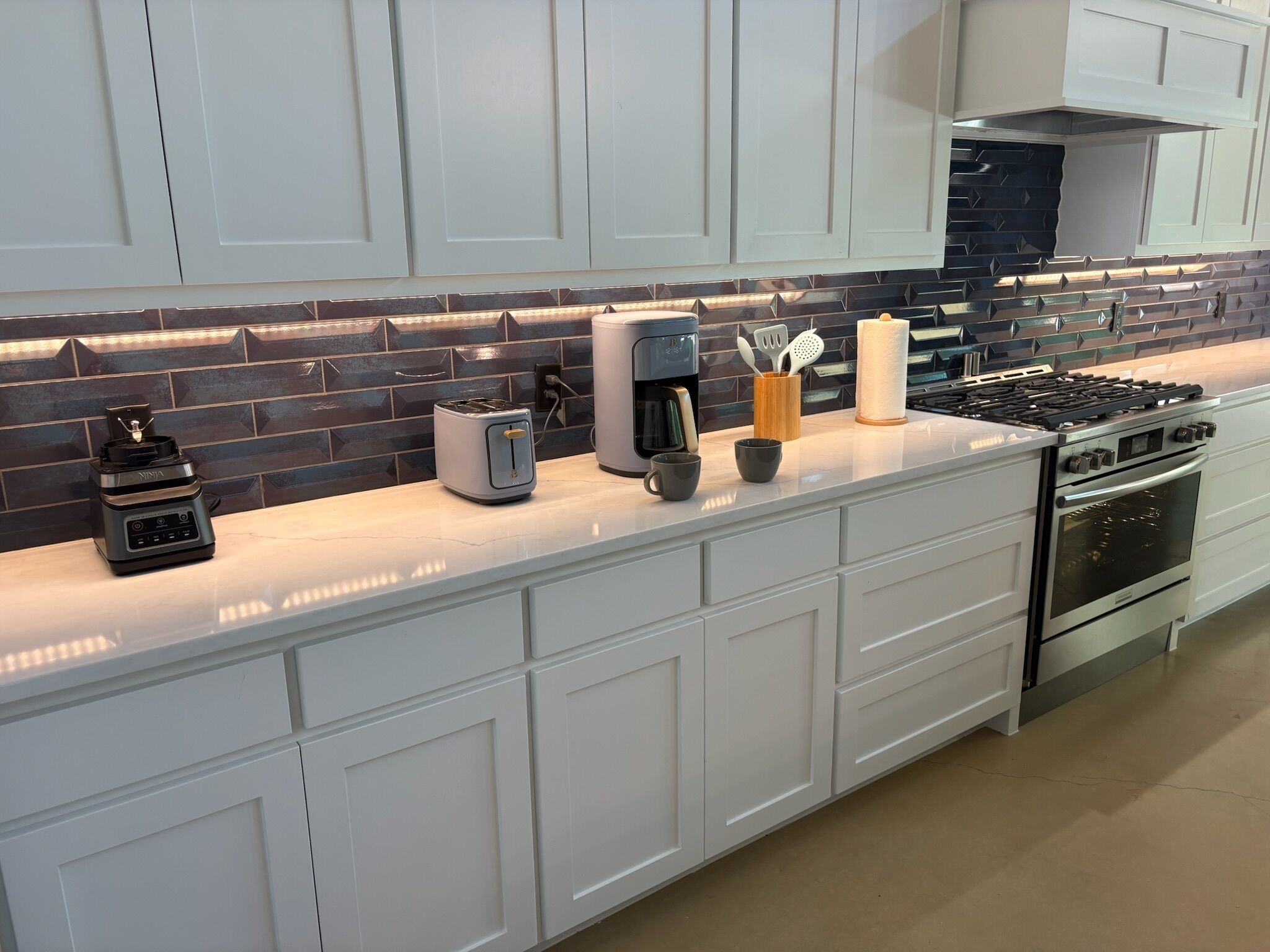 A modern kitchen with white cabinetry, a stainless steel stove, a coffee maker, and a toaster.