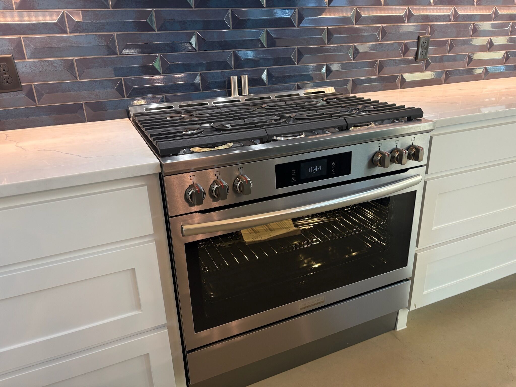 Uma cozinha com coifa de aço inoxidável, forno e painel de parede com padrões geométricos.