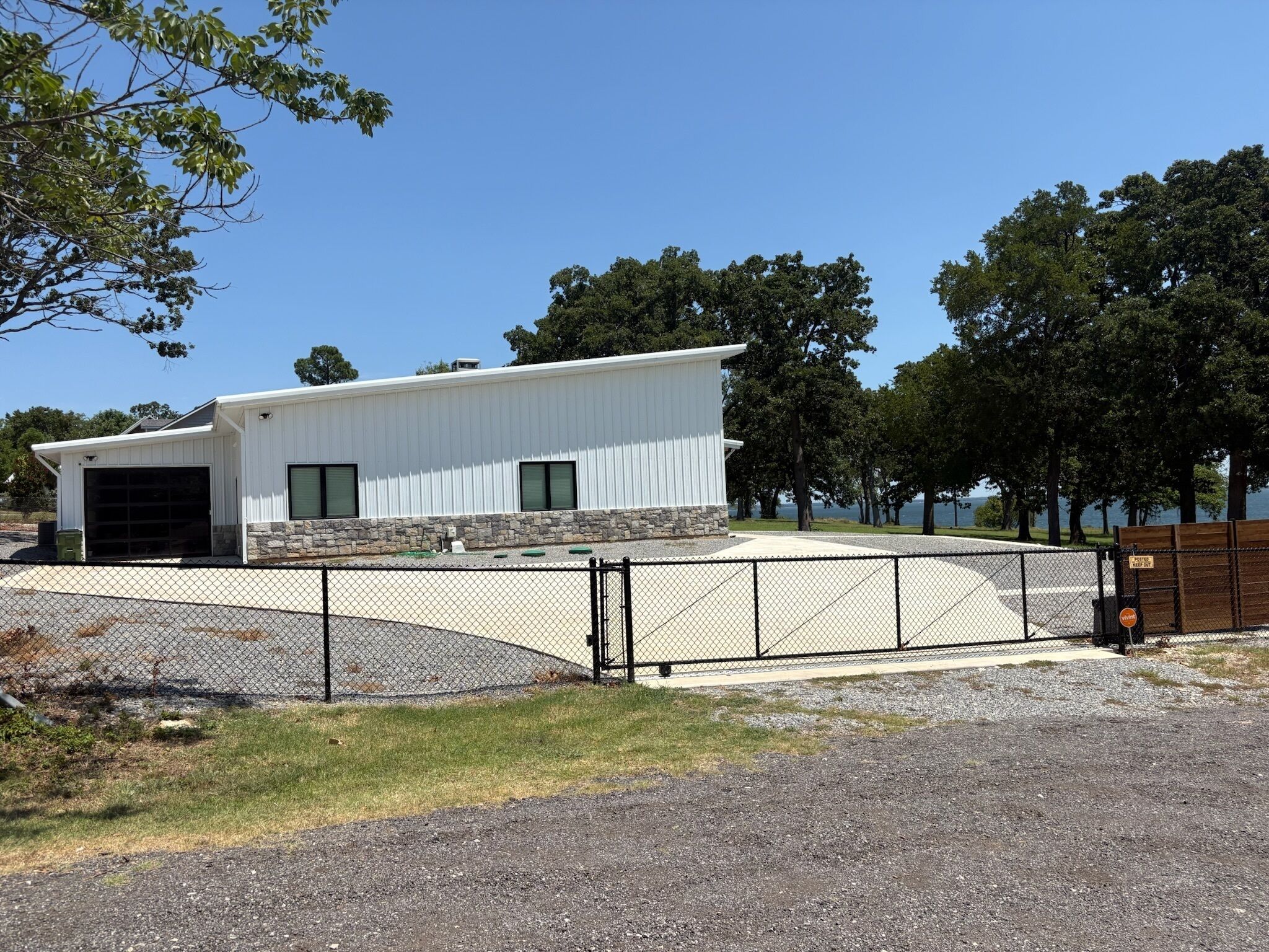 A single-story building with a garage, a stone foundation, and a fenced driveway.