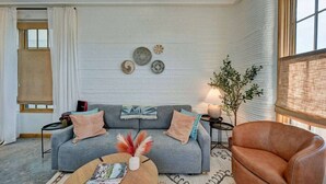 Un salón con un sofá gris, un sillón de cuero marrón, una mesa de centro con revistas y una planta.