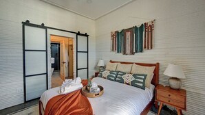 Un dormitorio con cama, mesitas de noche, una puerta corrediza y una pared con cortinas.