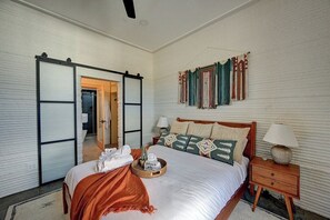 Ein Schlafzimmer mit einem Bett, Nachttischen, einer Schiebetür und einer Wand mit Vorhängen.
