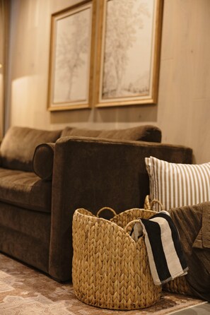 A brown sofa with a woven basket and a striped pillow in a room with framed artwork on the wall.