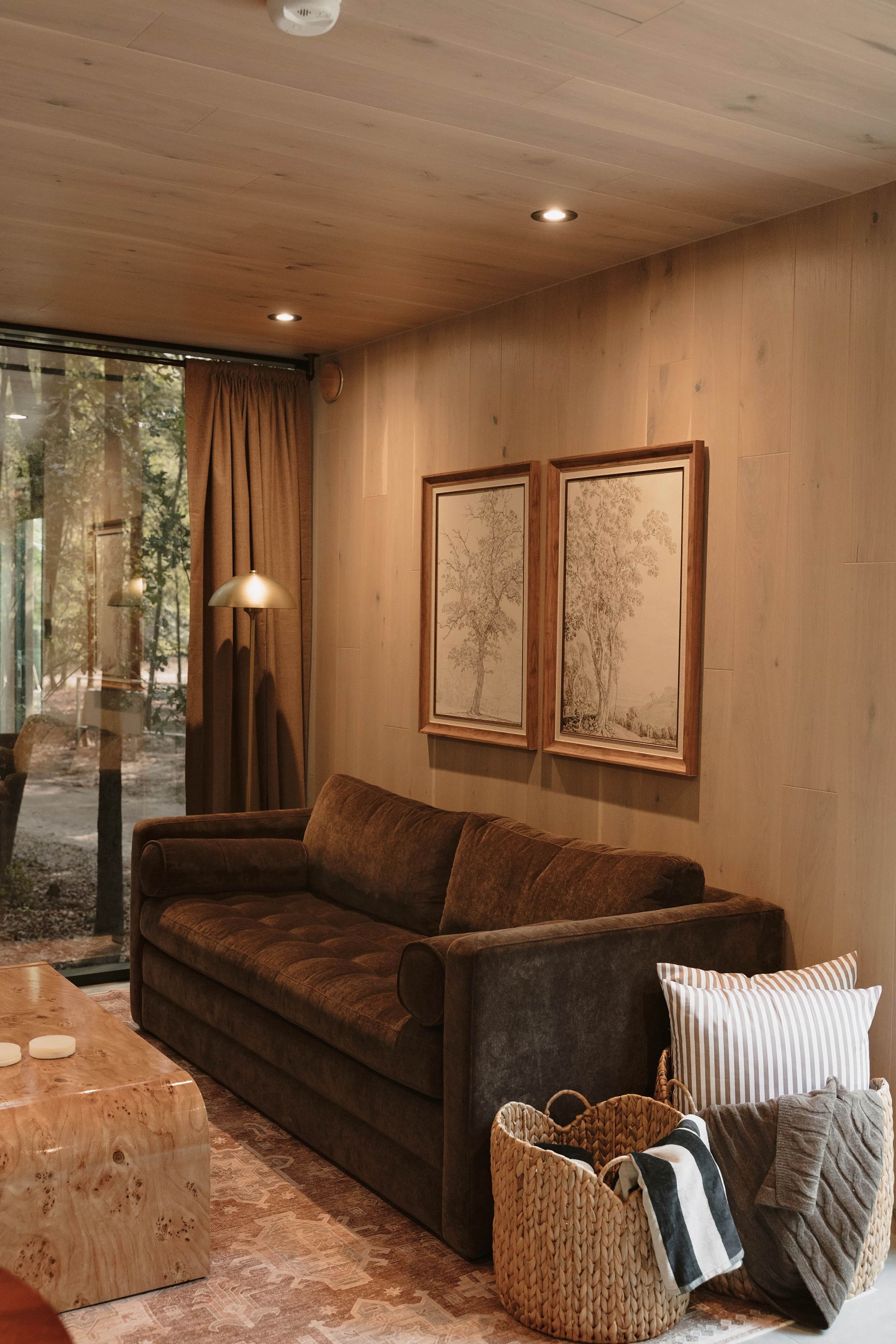 A cozy living room with a brown sofa, a lamp, and two framed artworks on the wall.