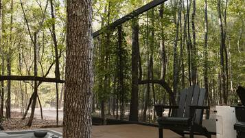 A wooden deck with a hot tub, a grill, and a seating area with chairs.