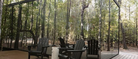 An outdoor wooden deck with Adirondack chairs and a small table, surrounded by a forest.