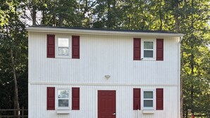 Un edificio de dos pisos con una puerta roja y ventanas, rodeado de árboles.