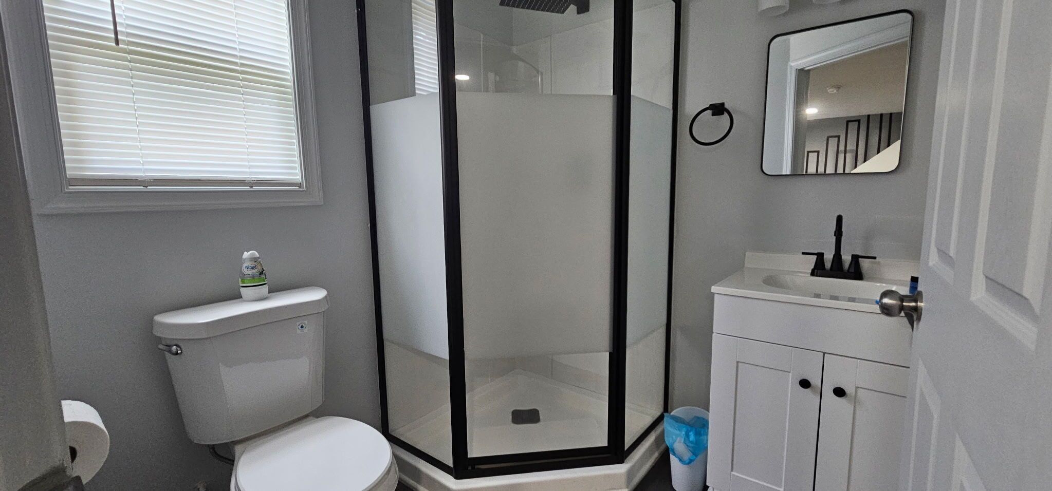 A bathroom with a toilet, a shower enclosure, a sink, and a mirror.