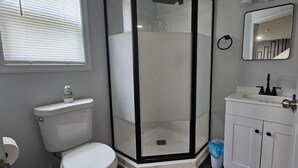 Un baño con inodoro, cabina de ducha, lavabo y espejo.